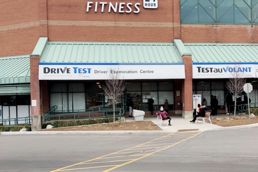 Exterior of an Ontario DriveTest Centre with bilingual signage and people waiting outside for driving exams.